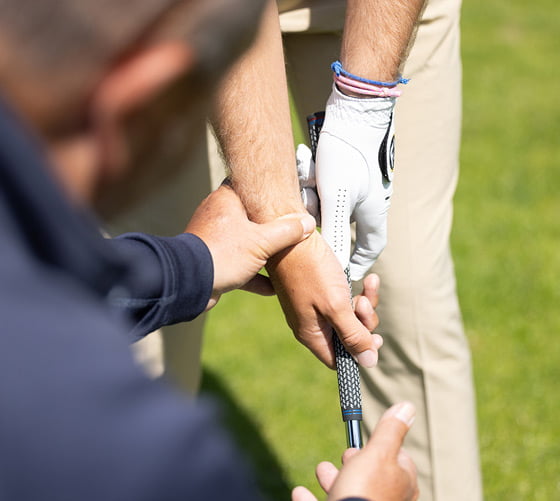 Een docent die iemand uitlegt hoe de golfclub vastgehouden dient te worden.